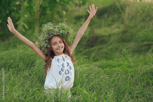 Cute little girl wearing wreath made of beautiful flowers in field