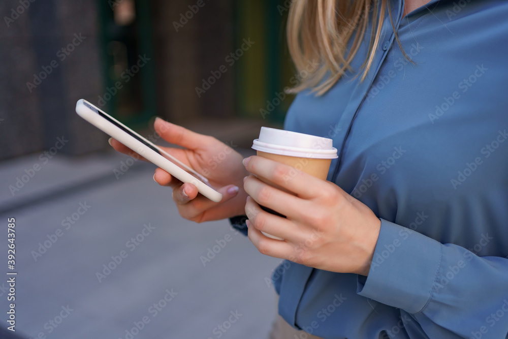 Beautiful young woman is using an app in her smartphone device to send a text message near business buildings