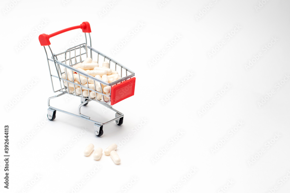 Pills and capsules in shopping cart on white background