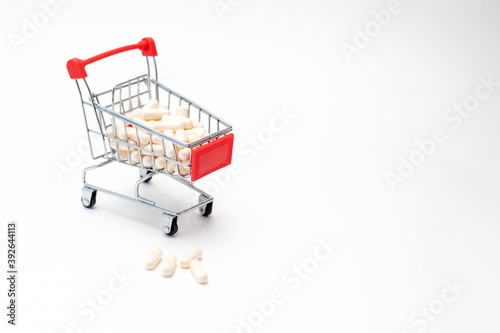 Pills and capsules in shopping cart on white background