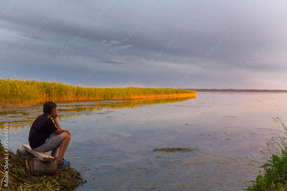 Teenboy sitting and relaxing on lake beach