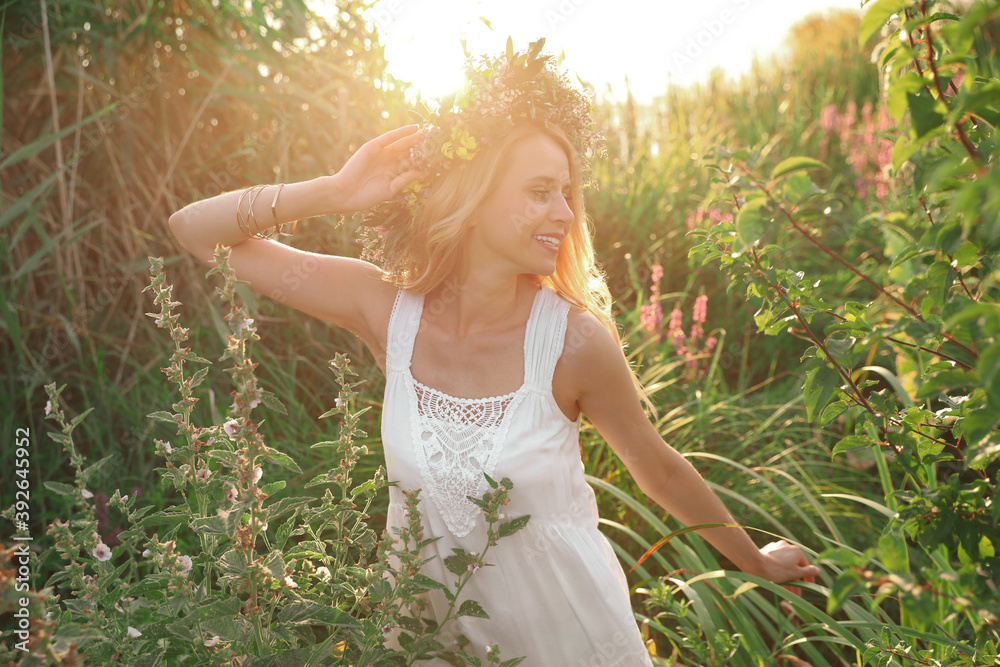 Young woman wearing wreath made of beautiful flowers outdoors on sunny day Young woman wearing wreath made of beautiful flowers outdoors on sunny day