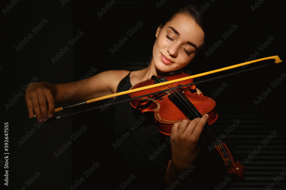 Beautiful young woman playing violin in dark room, focus on hand