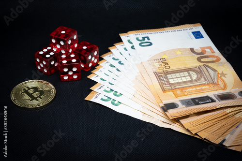Bitcoin coin, a pile of Euro banknotes and a few red cubes lie side by side on a dark background photo