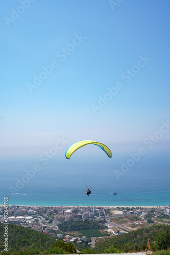 Orange paraglider flies over a mountain valley on a sunny summer day. Paragliding in the mountains in the sky