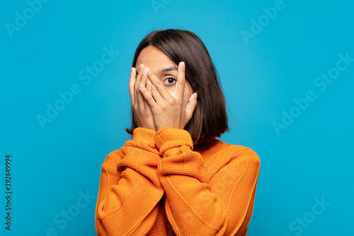 hispanic woman feeling scared or embarrassed, peeking or spying with eyes half-covered with hands