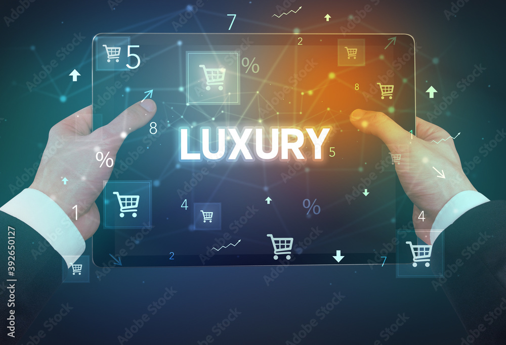 Close-up of a hand holding tablet with LUXURY inscription, online shopping concept