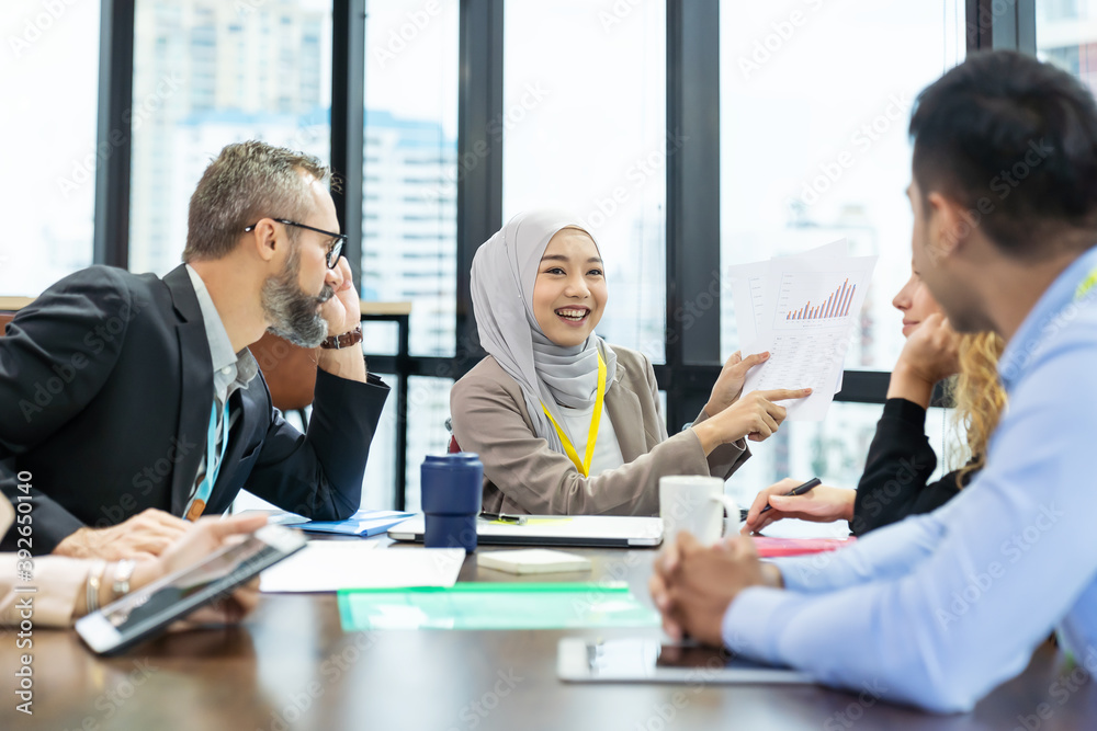 Asian Muslim business woman in hijab headscarf sitting on wheelchair presenting of her work to corporate colleagues in meeting in the modern office. diverse corporate colleagues and multicultural Asian Muslim business woman in hijab headscarf sitting on wheelchair presenting of her work to corporate colleagues in meeting in the modern office. diverse corporate colleagues and multicultural