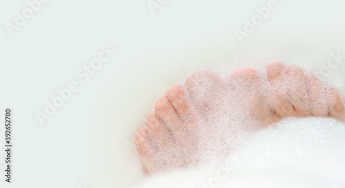 Woman legs, feet and toes in soap suds. Foam bath, relaxation, spa. Feet of a young girl in a thick foam, panoramic view, copy space. Toes