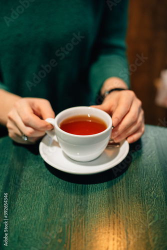 A cup of tea in hands on a green wooden table