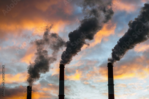 Three Smoking chimneys in dramatic colorful sky background. The concept of air pollution and the environment