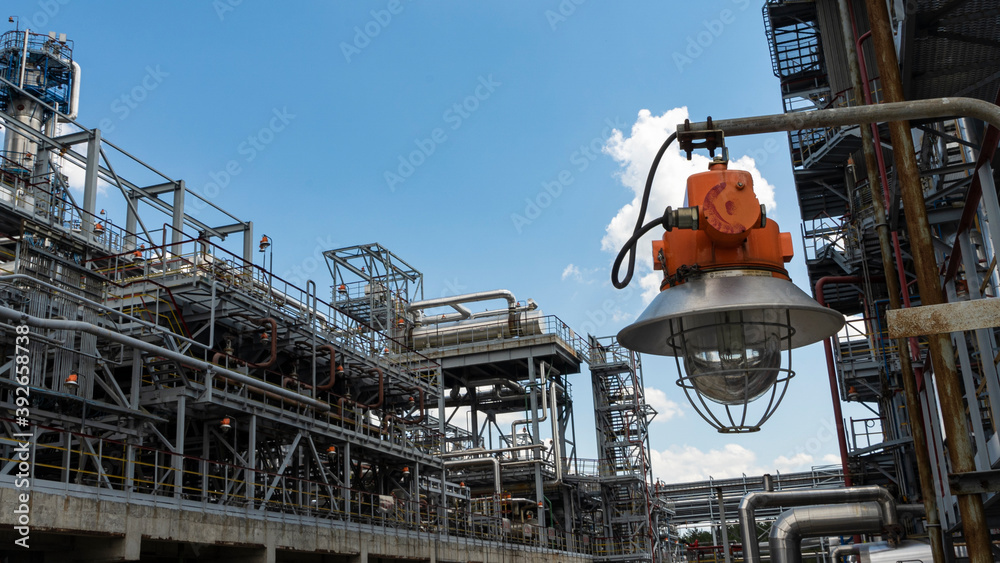 Industrial explosion proof lantern on the background of the refinery plant and classic blue sky. Space for text.