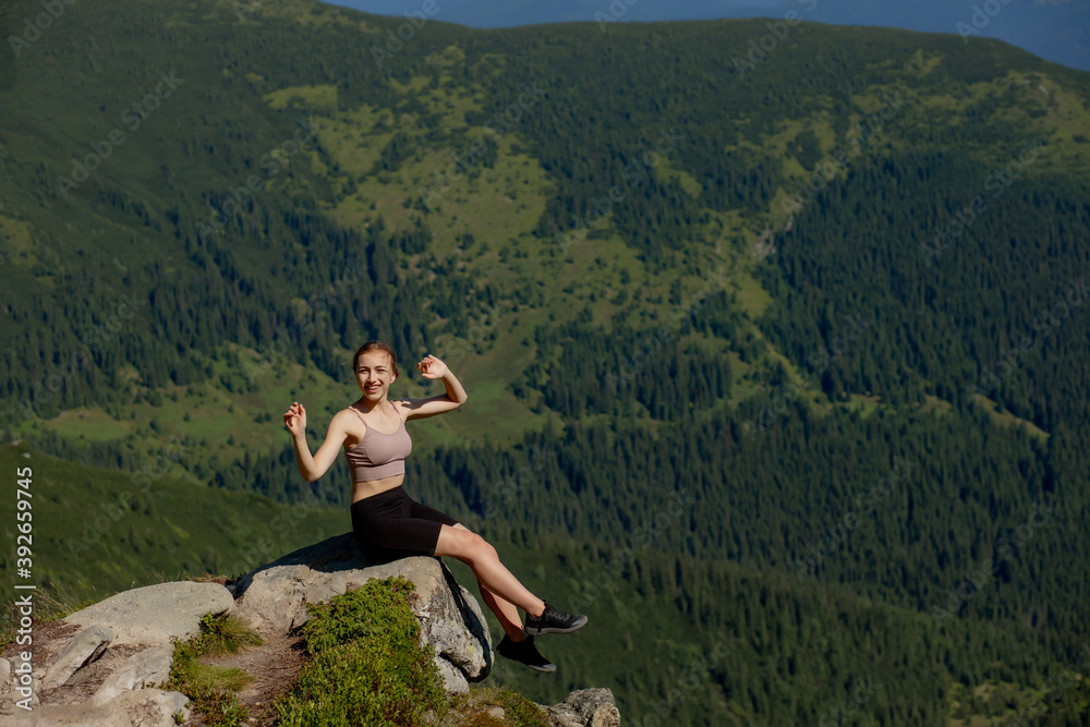 Naklejka premium A woman sits on the edge of the cliff and looking at the sun valley and mountains