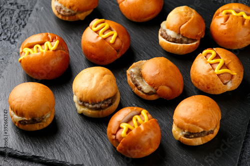 Mini hamburgers, burger and hot dogs with yellow mustard on black slate board © grinchh