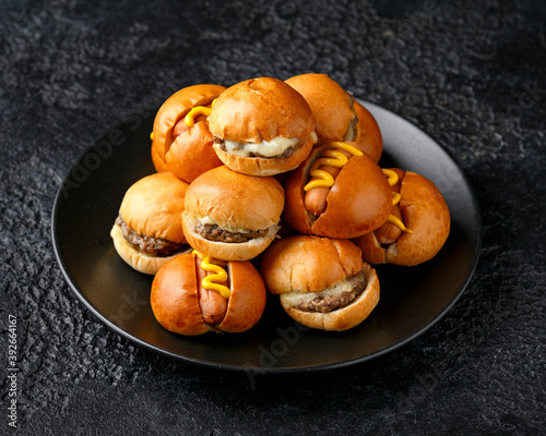 Принти на полотні Mini hamburgers, burger and hot dogs with yellow mustard on black plate