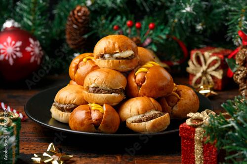 Christmas mini hamburgers, burger and hot dogs with decoration, gifts, green tree branch on wooden rustic table