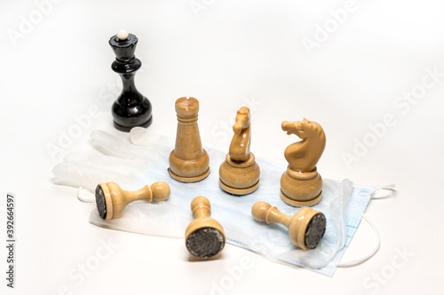 wooden chess pieces on a medical mask. Black's Queen is watching from afar