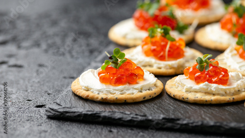 Salmon caviar and soft cheese savory crackers with sesame and poppy seeds served on black slate board