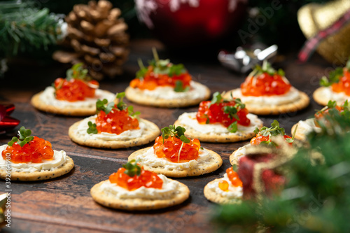 Salmon caviar and soft cheese savory crackers with decoration, gifts, green tree branch on wooden rustic table.