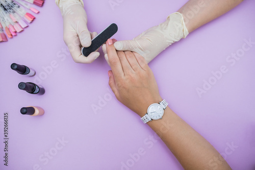 the master makes a manicure for the client. Manicure. The manicurist saws the nails for the client. Make a manicure, close-up, on a lilac background, top view