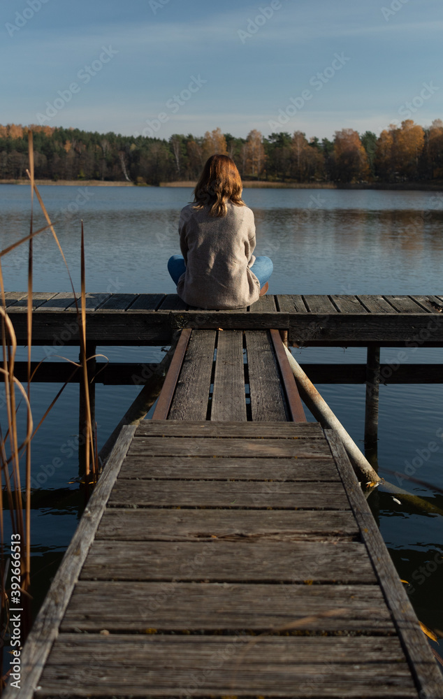 Attractive young female sitting on top of a pier while witnessing the Galve lake in Trakai, Lithuania. Trakai was the ancient capital of this baltic republic.