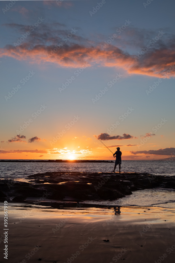 Silhouette of man fishing on the sea coast at sunset