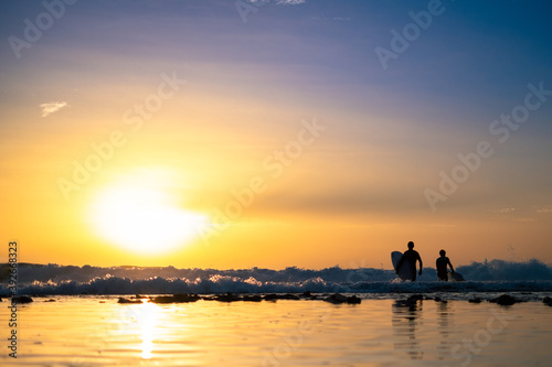 Silhouettes of two men surfing at sunset
