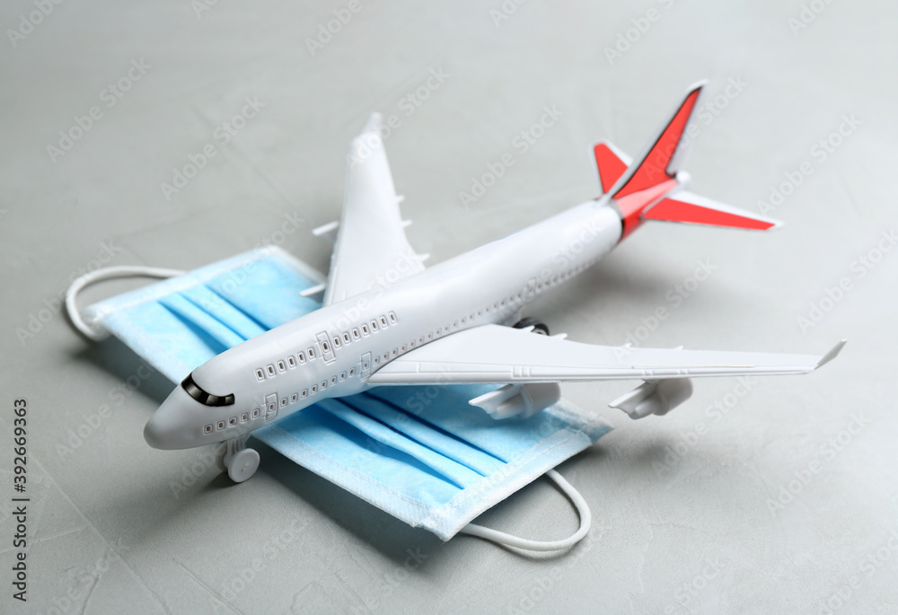 Toy airplane and medical mask on grey stone background, closeup. Travelling during coronavirus pandemic Toy airplane and medical mask on grey stone background, closeup. Travelling during coronavirus pandemic