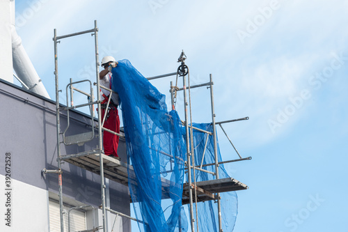 obrero sobre un andamio de obra extendiendo una red de seguridad sobre la fachada