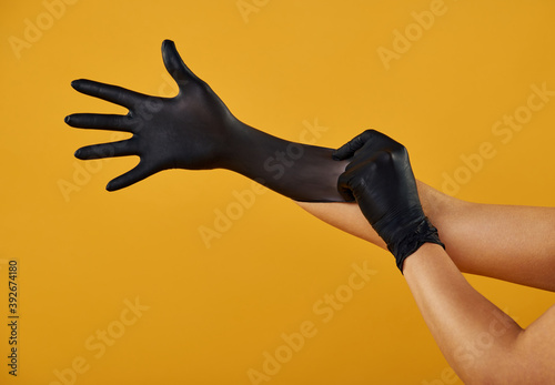 Isolated hands on a yellow background wear black latex medical gloves.