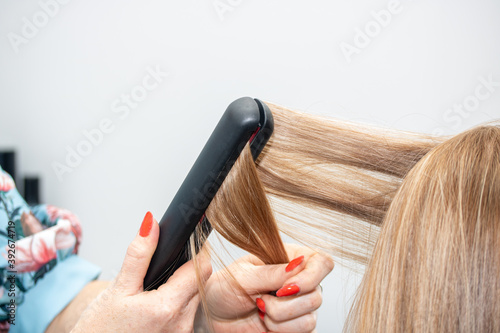 Barber straightens long hair with a hair iron, close-up.