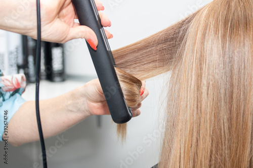 Barber curls long hair with a hair iron  close-up.