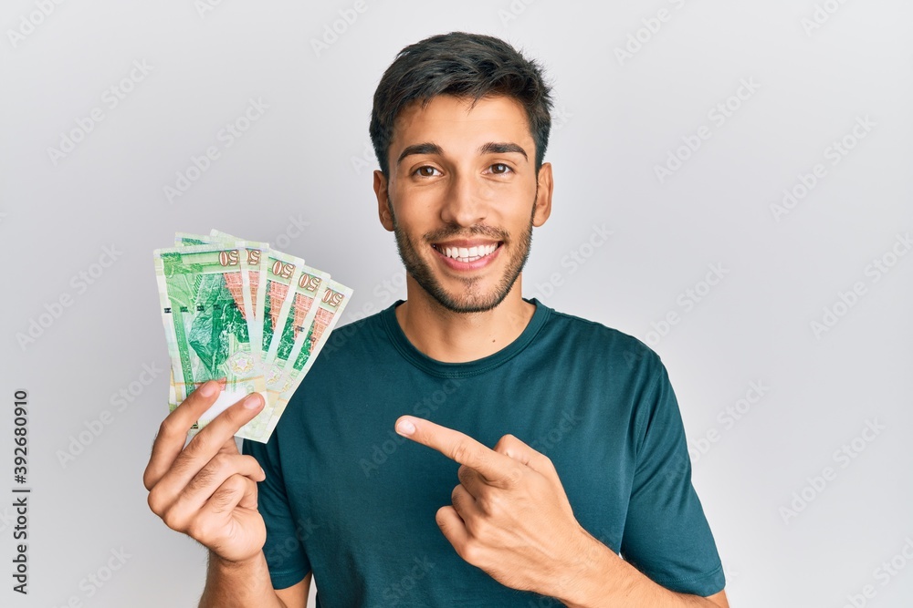 Young handsome man holding 50 hong kong dollars banknotes smiling happy pointing with hand and finger Young handsome man holding 50 hong kong dollars banknotes smiling happy pointing with hand and finger