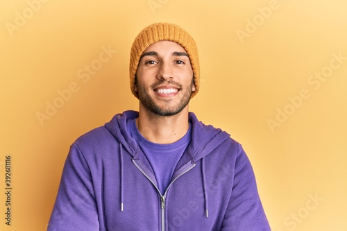 Young handsome man wearing wool winter hat happy face smiling with crossed arms looking at the camera. positive person.