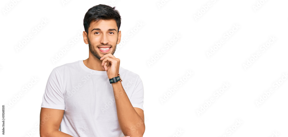 Young handsome man wearing casual white tshirt looking confident at the camera with smile with crossed arms and hand raised on chin. thinking positive. Young handsome man wearing casual white tshirt looking confident at the camera with smile with crossed arms and hand raised on chin. thinking positive.