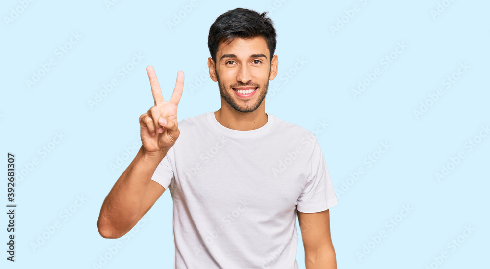 Young handsome man wearing casual white tshirt showing and pointing up with fingers number two while smiling confident and happy. Young handsome man wearing casual white tshirt showing and pointing up with fingers number two while smiling confident and happy.