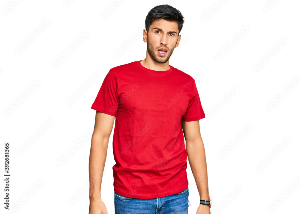 Fototapeta premium Young handsome man wearing casual red tshirt in shock face, looking skeptical and sarcastic, surprised with open mouth