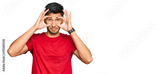 Young handsome man wearing casual red tshirt trying to open eyes with fingers, sleepy and tired for morning fatigue