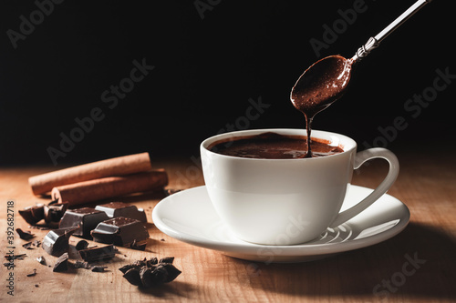 Liquid hot chocolate flow from spoon into cup on a wooden table with dark background