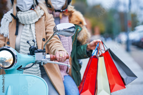 Two women wearing masks and holding shopping bags on scooter