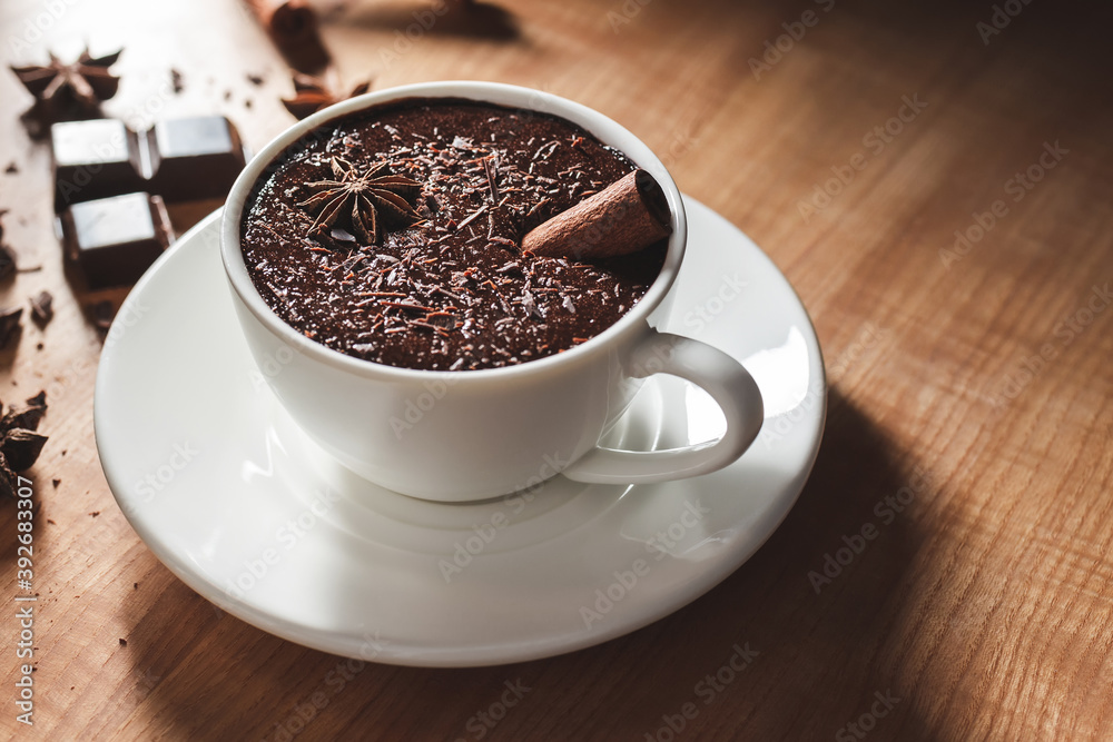 Fototapeta premium Hot chocolate drink in white cup, broken chocolate, cinnamon stick and star anise on a wooden table