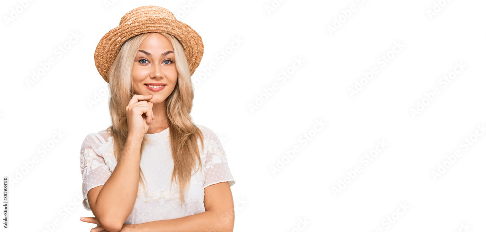 Young blonde girl wearing summer hat looking confident at the camera with smile with crossed arms and hand raised on chin. thinking positive. Young blonde girl wearing summer hat looking confident at the camera with smile with crossed arms and hand raised on chin. thinking positive.