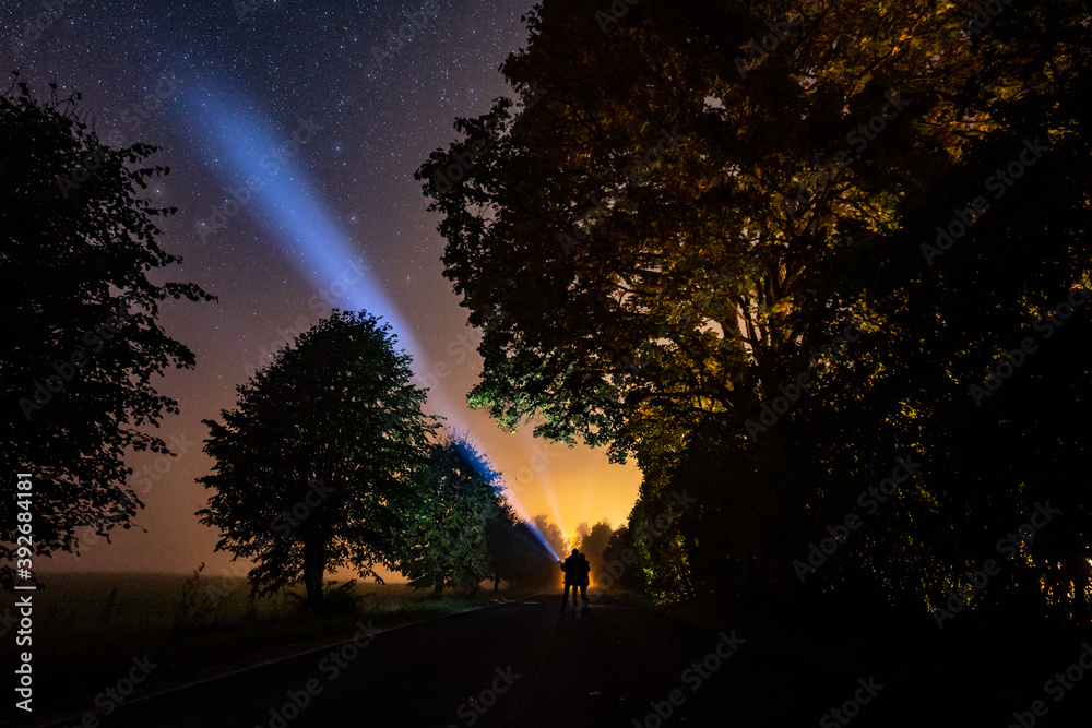 Overhead milky way with stars in clear summer night. Country side. Young couple standing with bright torch light.