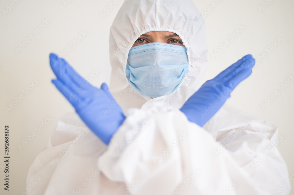 Fototapeta premium Female doctor in a protective suit shows a stop with crossed arms. Stop the coronavirus