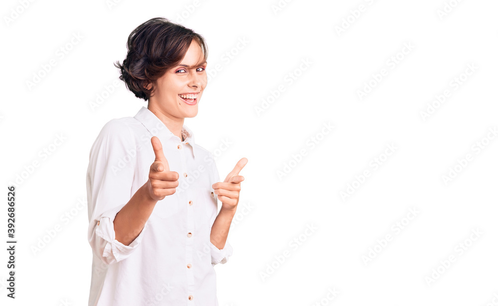 Beautiful young woman with short hair wearing elegant white shirt pointing fingers to camera with happy and funny face. good energy and vibes. Beautiful young woman with short hair wearing elegant white shirt pointing fingers to camera with happy and funny face. good energy and vibes.