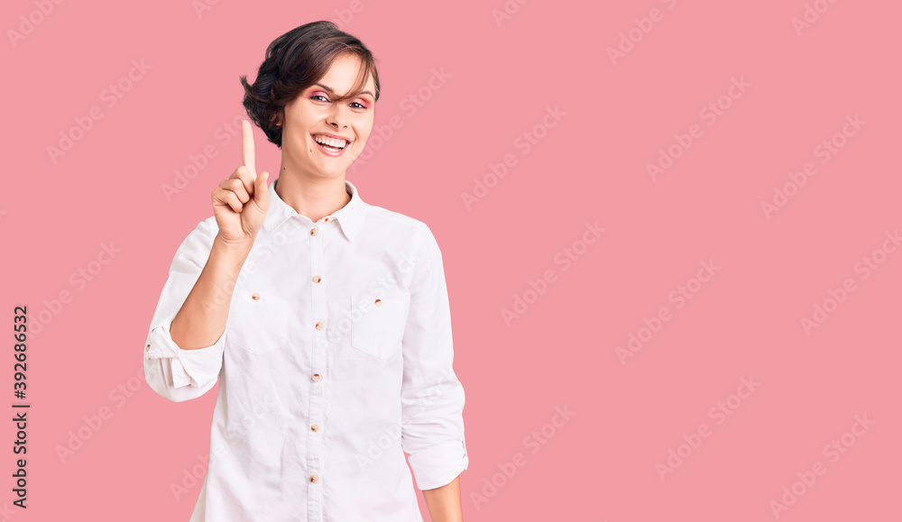 Beautiful young woman with short hair wearing elegant white shirt showing and pointing up with finger number one while smiling confident and happy. Beautiful young woman with short hair wearing elegant white shirt showing and pointing up with finger number one while smiling confident and happy.