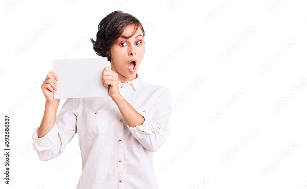 Beautiful young woman with short hair holding blank empty banner scared and amazed with open mouth for surprise, disbelief face Beautiful young woman with short hair holding blank empty banner scared and amazed with open mouth for surprise, disbelief face