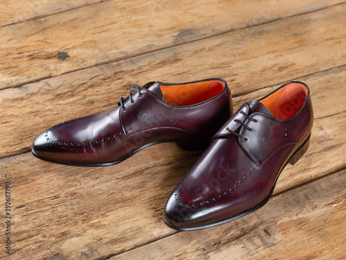 Wine-colored leather shoes with orange trim on the inside against a wooden surface from old boards