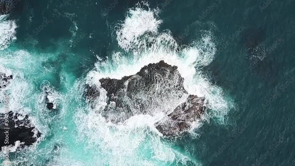 Slow motion aerial of waves surging over rock shelf in deep aqua blue ocean