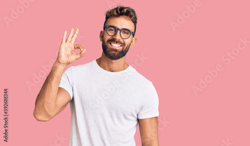 Young hispanic man wearing casual clothes and glasses smiling positive doing ok sign with hand and fingers. successful expression.